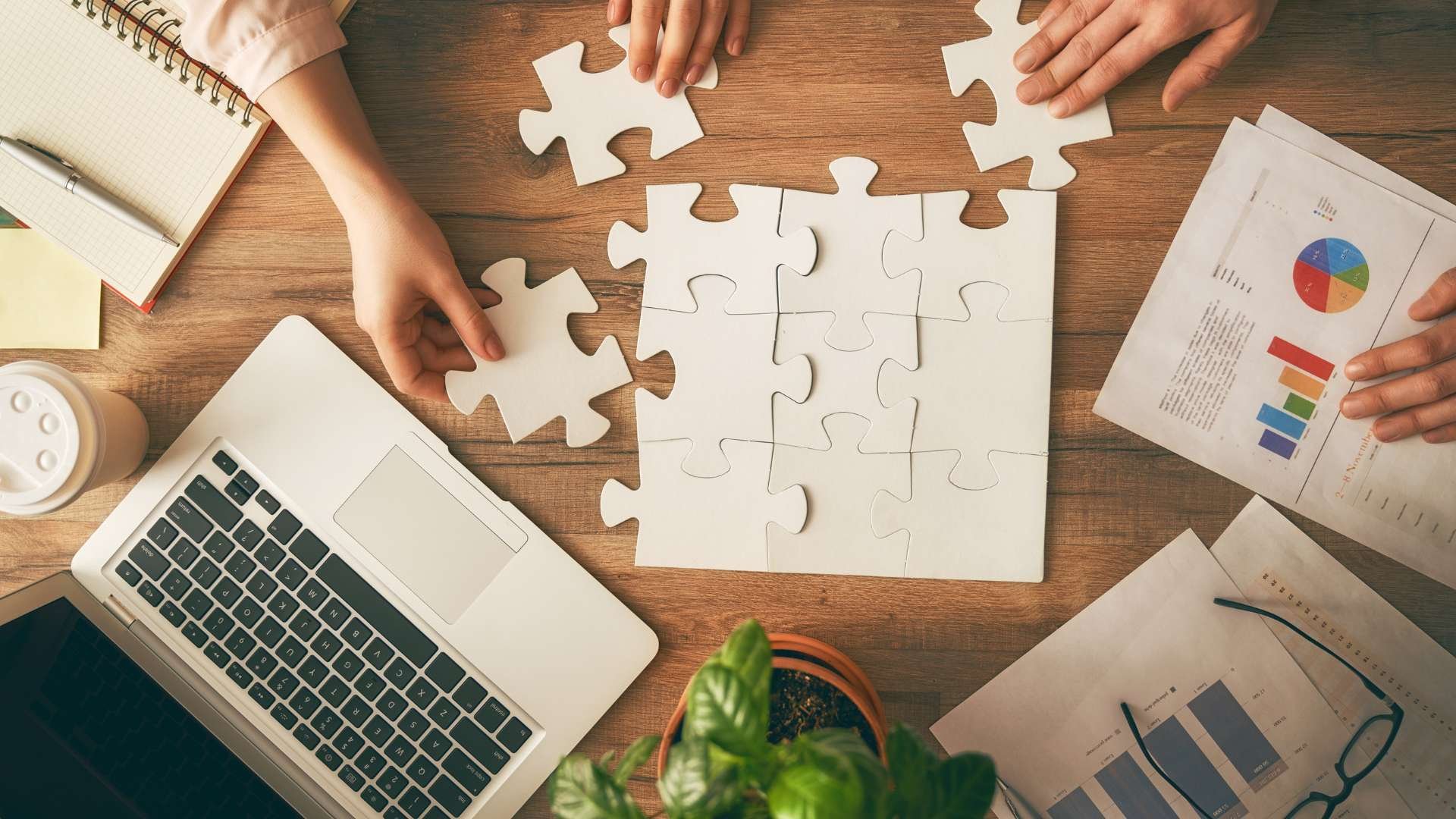 Hands assembling a jigsaw puzzle beside a laptop and business reports, symbolizing Fluid IT's versatile solutions tailored to Dallas business goals.