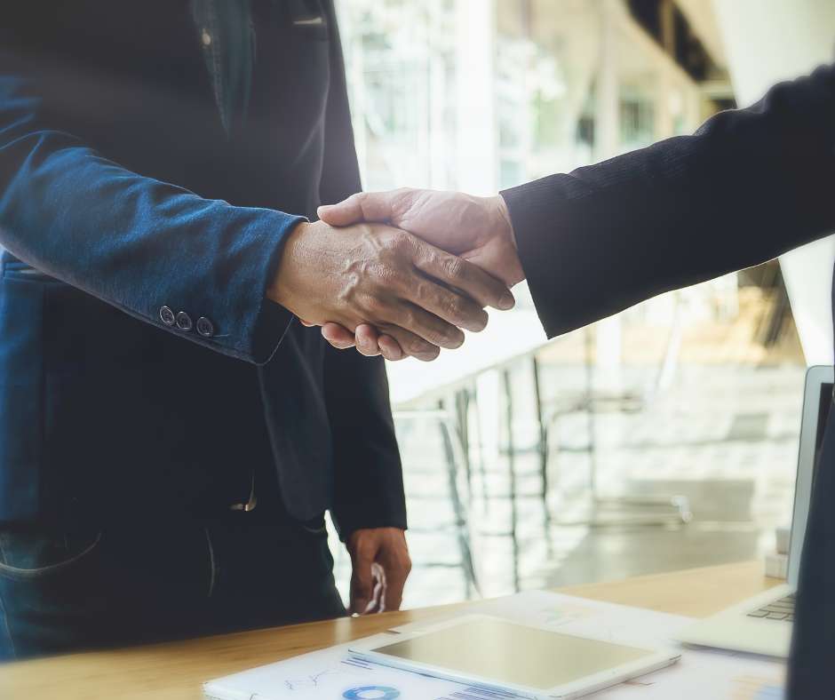 Two professionals shaking hands over a workspace, symbolizing the strong, dedicated partnerships Fluid IT forms with Frisco businesses.