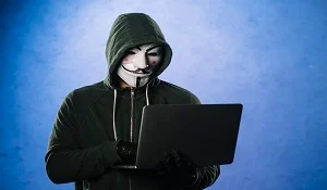Male hoodie hacker wearing myster mask and using laptop. Ransomeware cyber attack or Internet security concept.